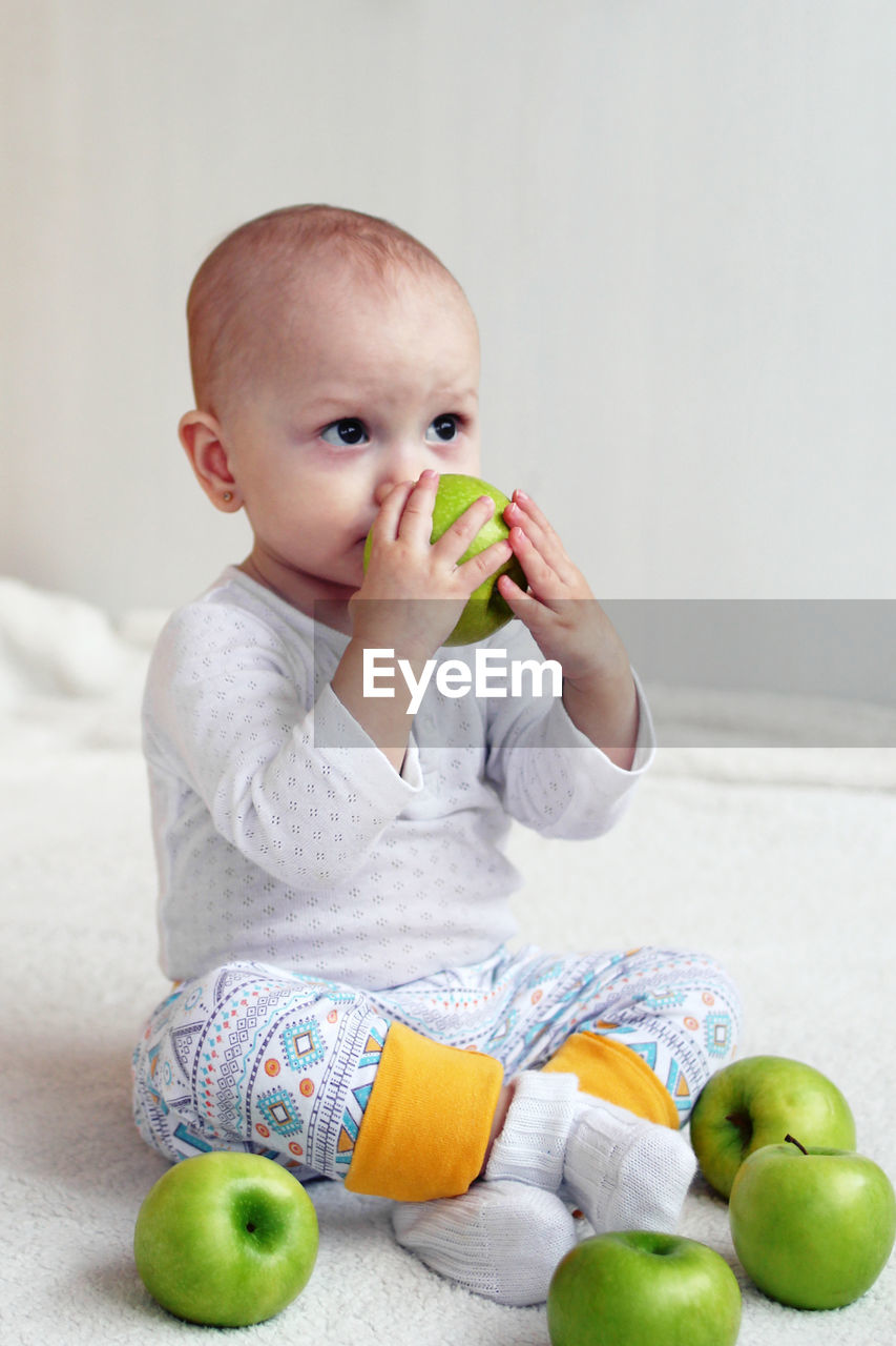 High angle view of cute baby girl sitting on carpet with apple at home