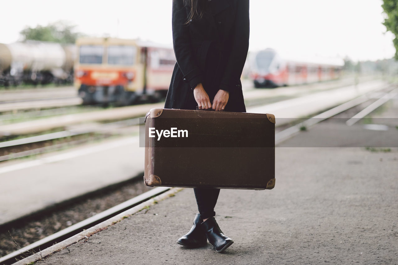 Low section of woman carrying suitcase while standing on railroad station platform