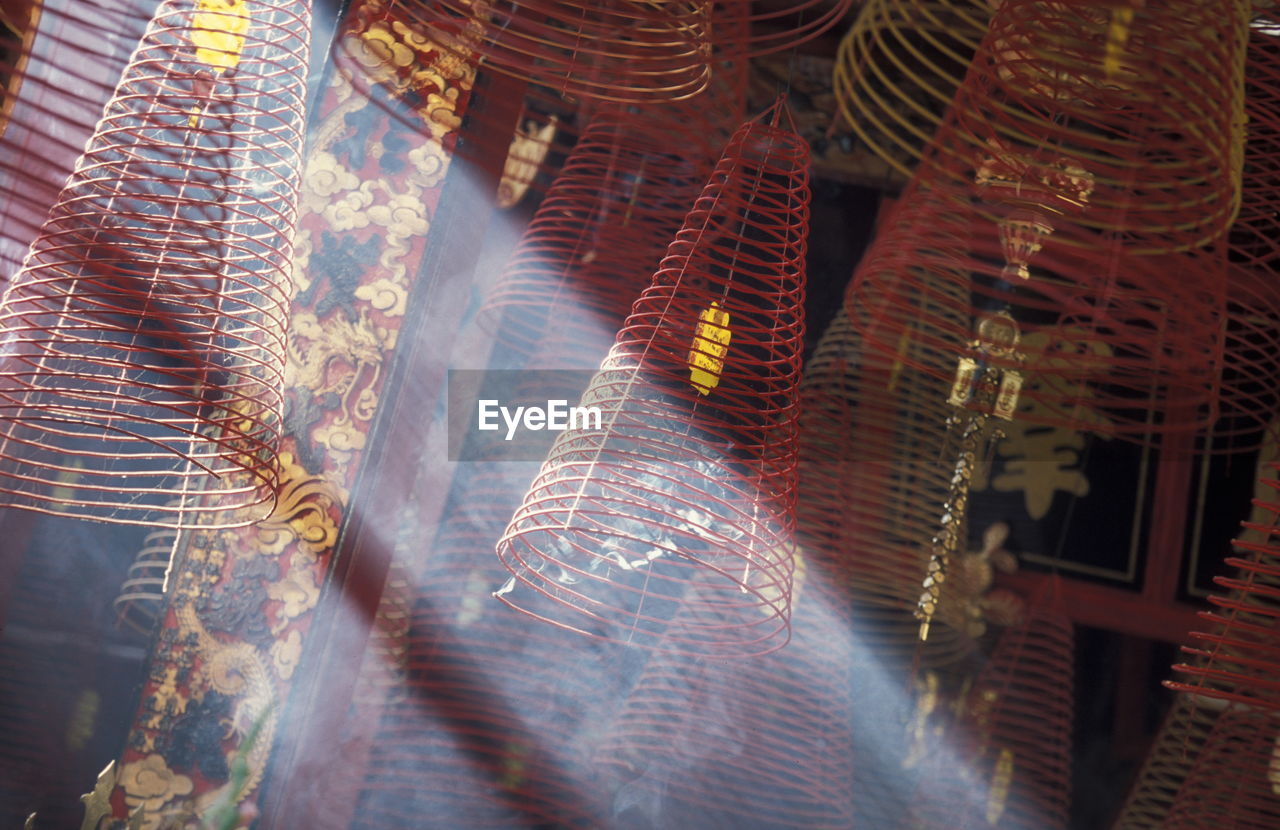 Low angle view of sunlight streaming by spiral incense sticks in temple