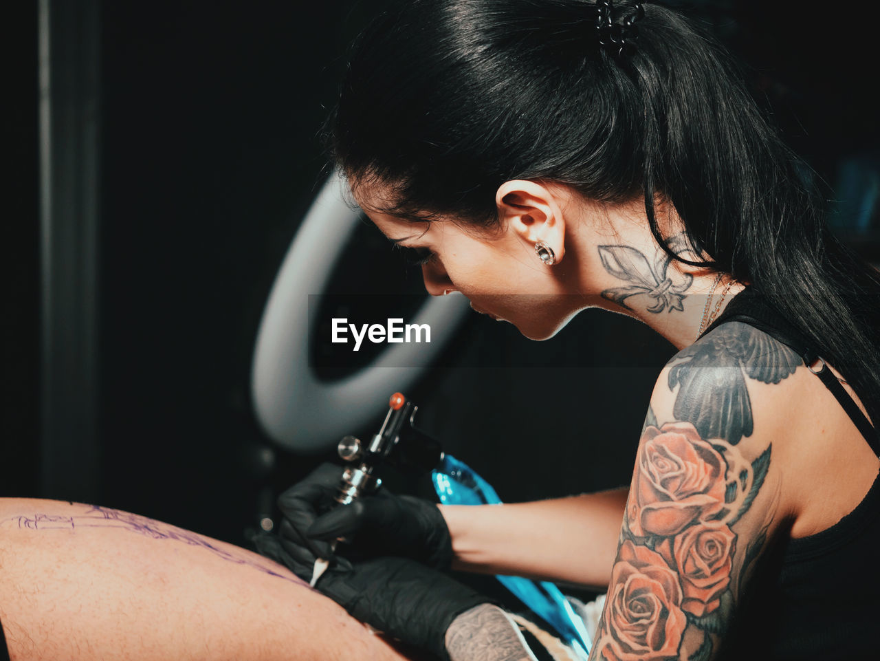 Young woman tattooing statue of liberty man on calf at parlor