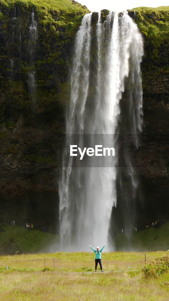 Scenic view of waterfall with woman standing on grass