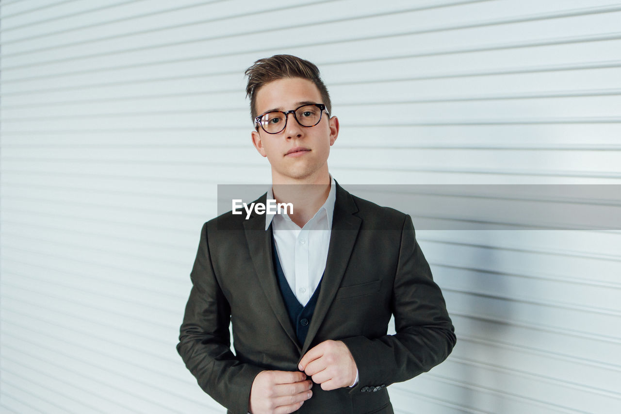 Portrait of handsome man wearing suit standing by white wall