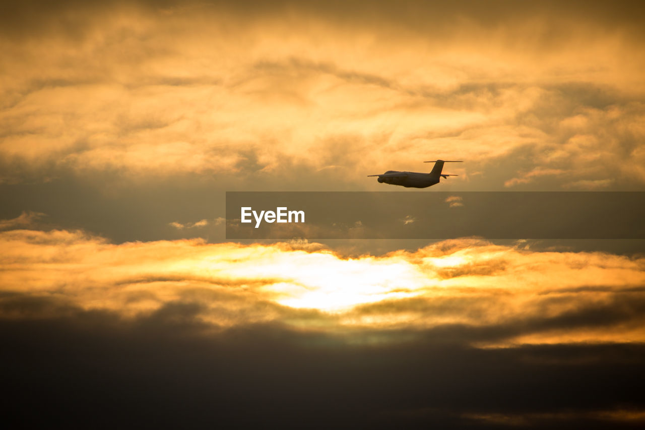Low angle view of airplane flying against cloudy sky during sunset