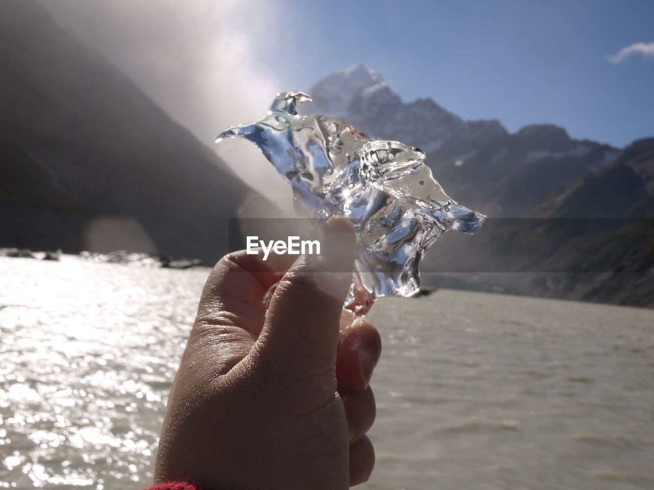 Close-up of person holding ice against lake and mountains