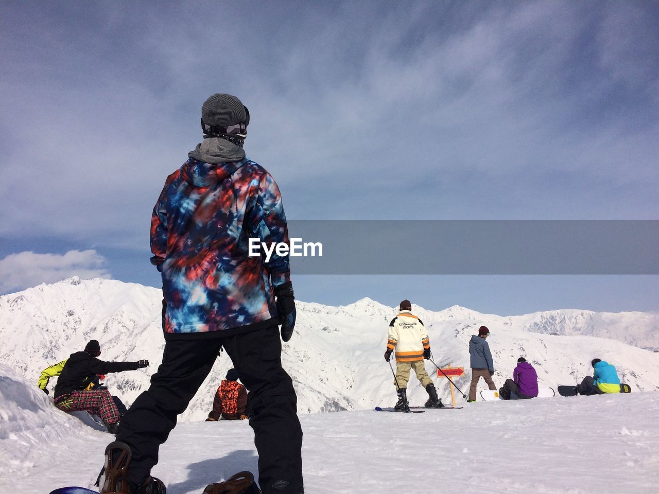 People at snow covered field by mountains against sky