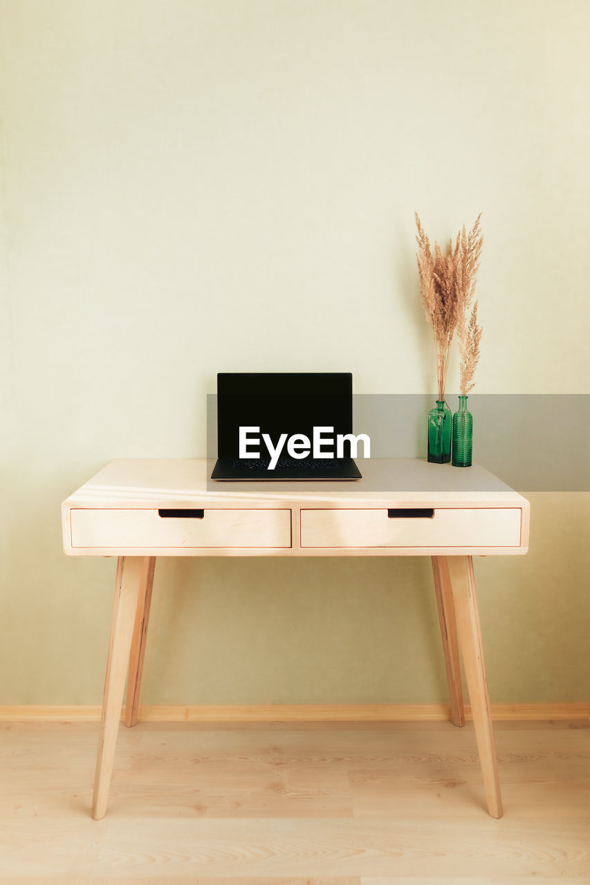 Black laptop on wooden table in home interior. empty wall with copyspace.