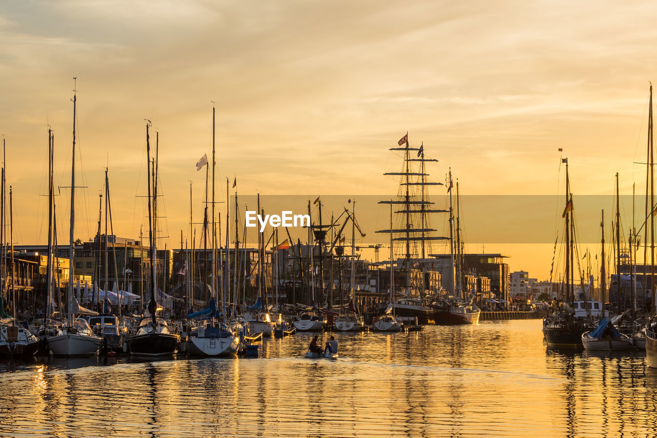 Sailboats moored at harbor against sky during sunset