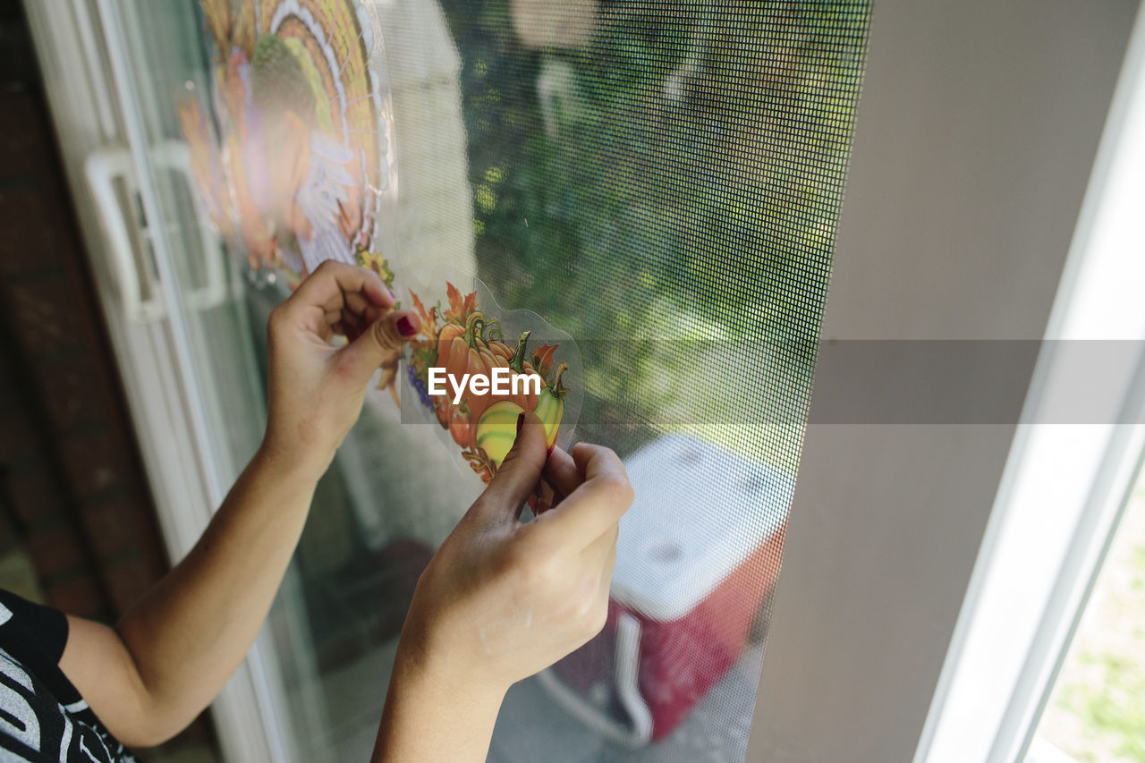 Cropped hands of girl sticking fruits label on window glass at home