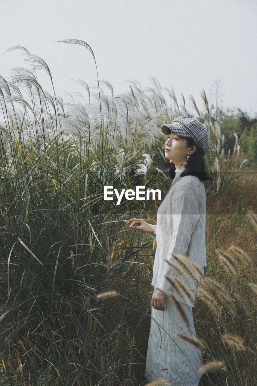 Side view of young woman standing on field against sky