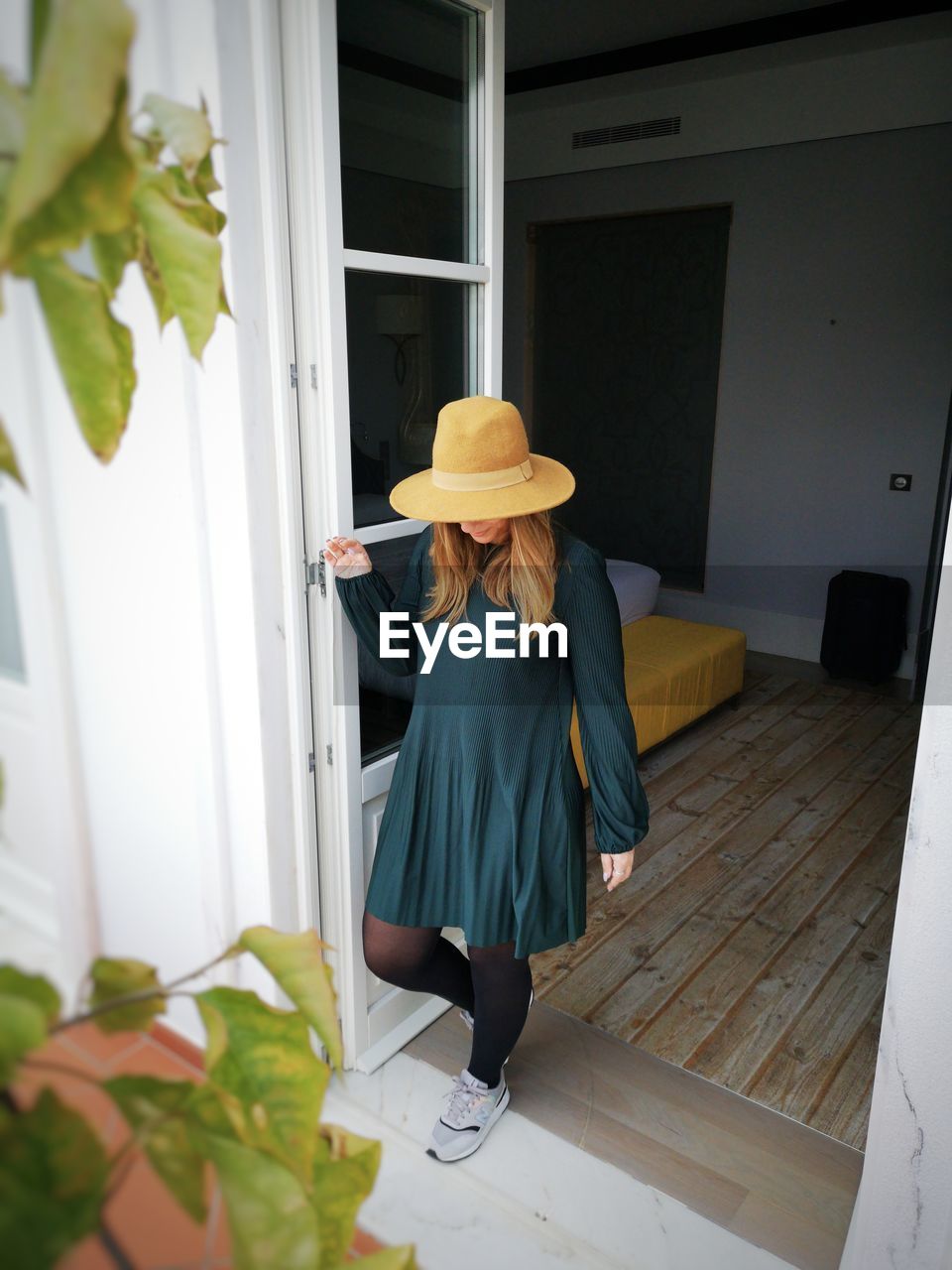 REAR VIEW OF WOMAN WEARING HAT STANDING AGAINST DOOR