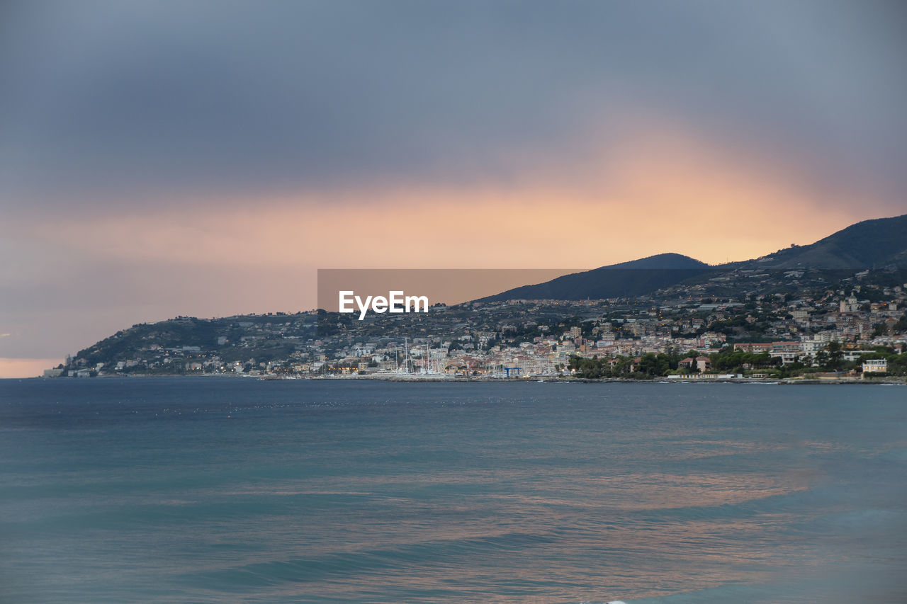 SEA BY CITY AGAINST SKY AT SUNSET