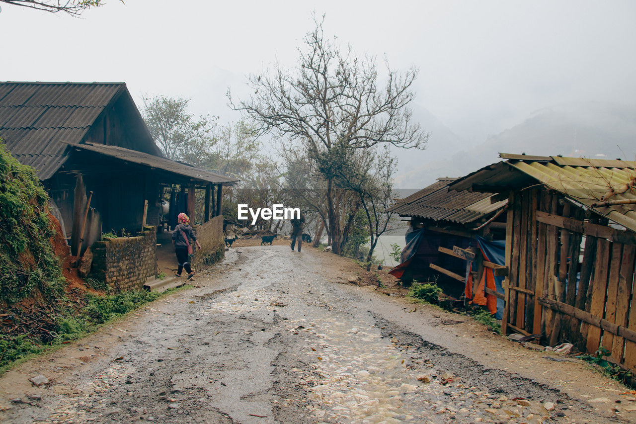 rural area, architecture, village, shack, building exterior, building, built structure, house, tree, nature, sky, plant, residential district, transport, road, rural scene, hut, landscape, town, outdoors, the way forward, transportation, day, men, adult, dirt road, city, wood