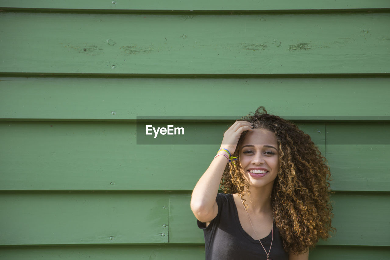 Portrait of smiling young woman standing against wall