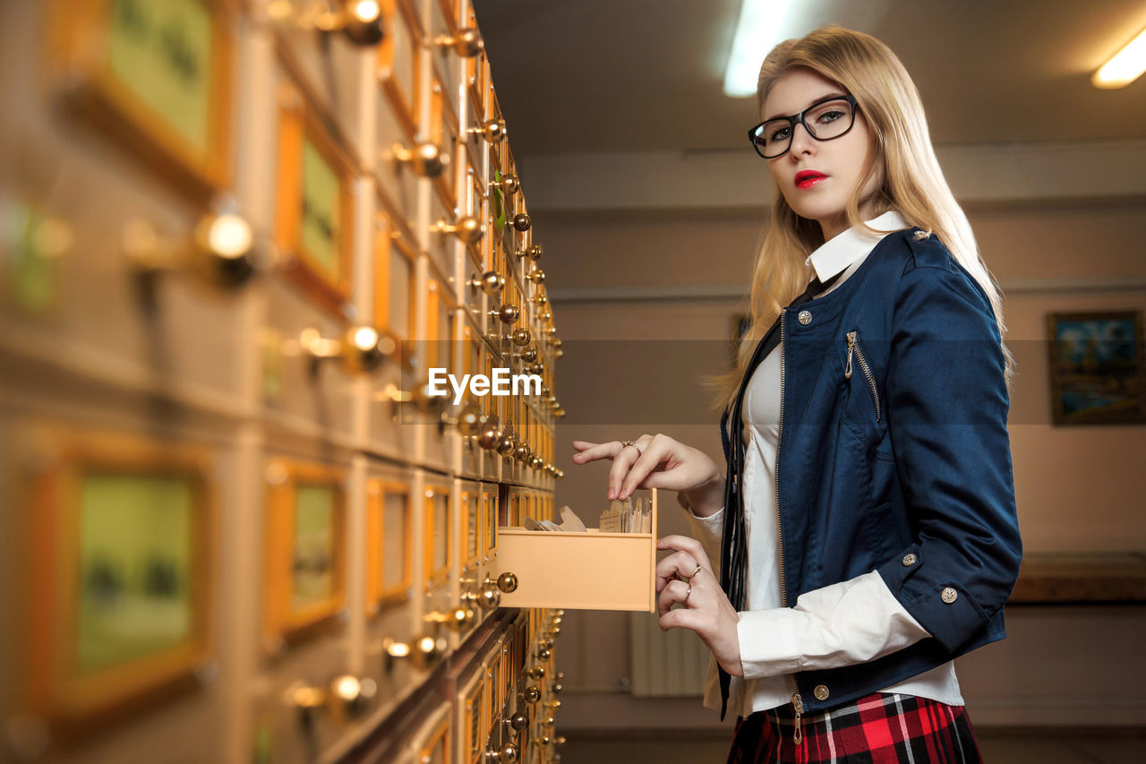 Portrait of young woman standing by drawers