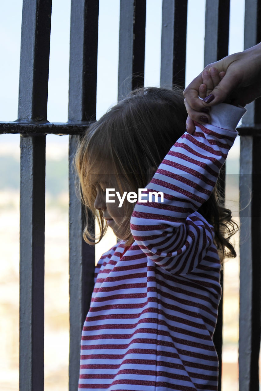 Cropped image of mother holding daughter hand by fence