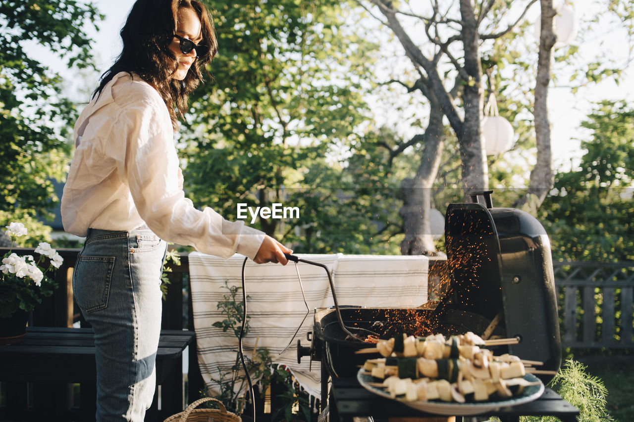 Woman grilling food on barbecue at yard during summer