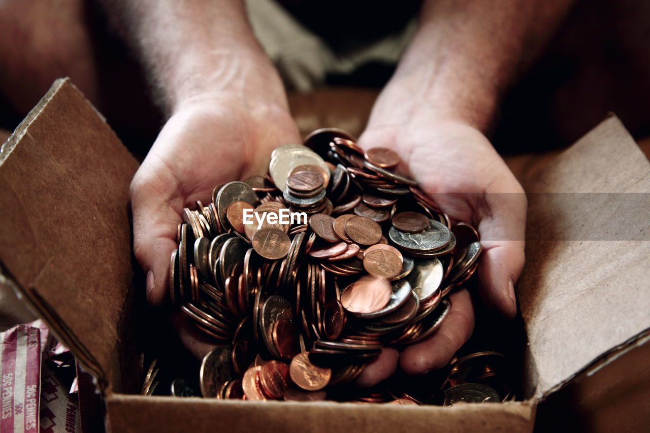 Close-up of man putting us coins in cardboard box