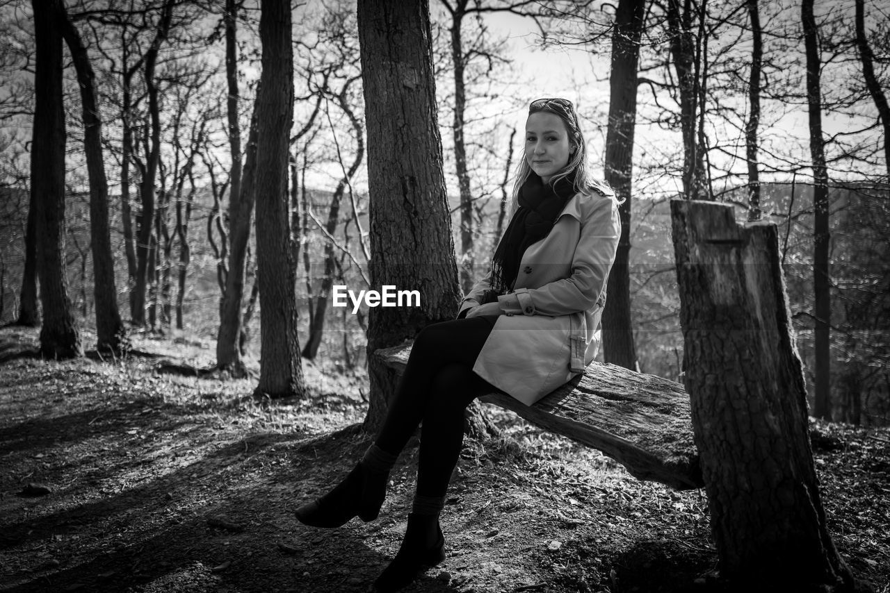 Portrait of woman sitting on bench against bare trees in forest