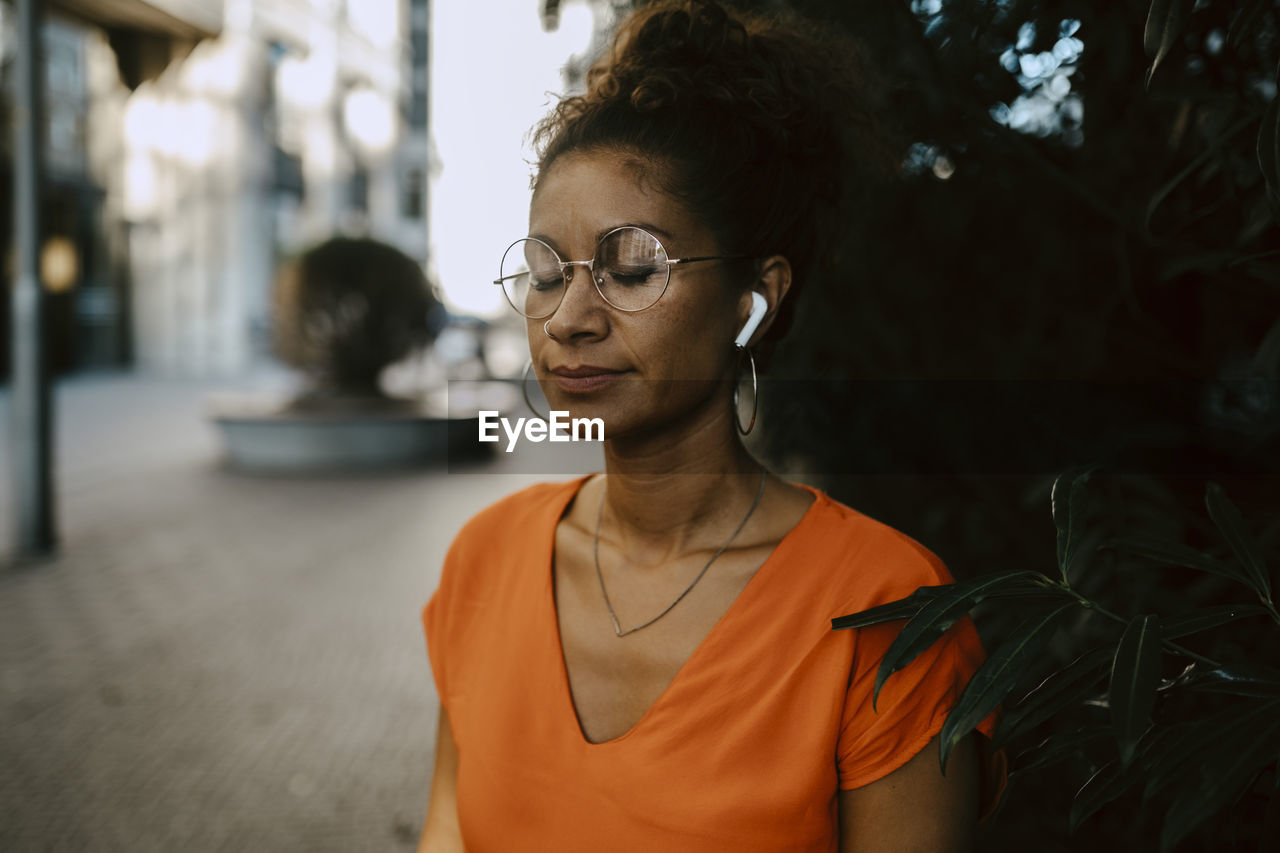 Female entrepreneur listening music through wireless earphones on footpath