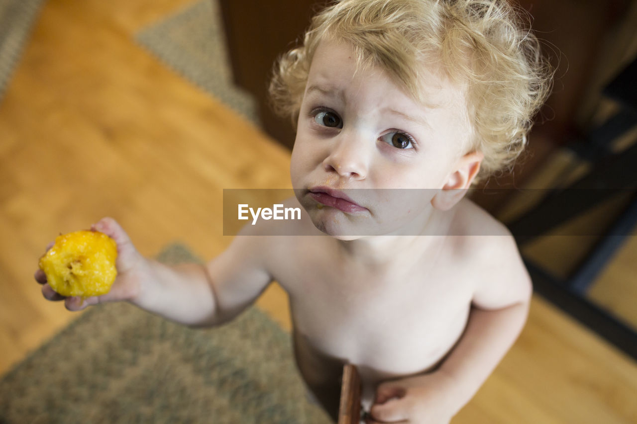 Guilty looking young toddler holds up a half eaten peach