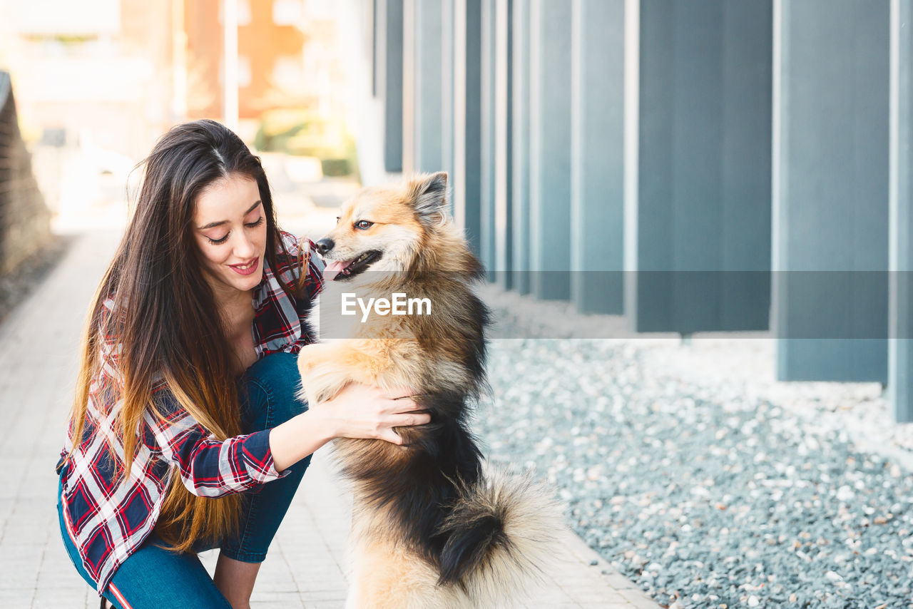 Woman playing with dog on footpath