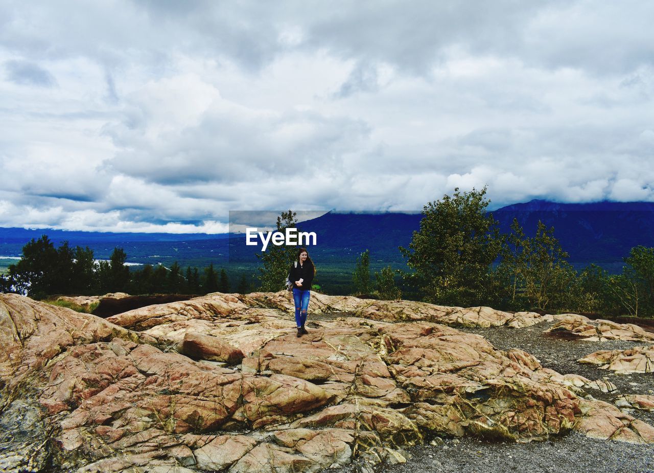 REAR VIEW OF MEN WALKING ON ROCKS AGAINST SKY