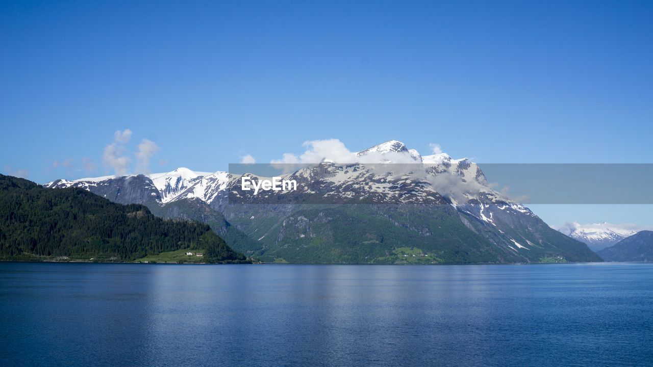 Scenic view of sea and snowcapped mountains against blue sky