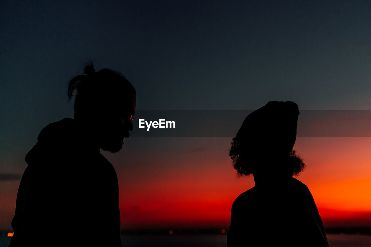 Silhouette of couple standing at beach against clear sky during sunset