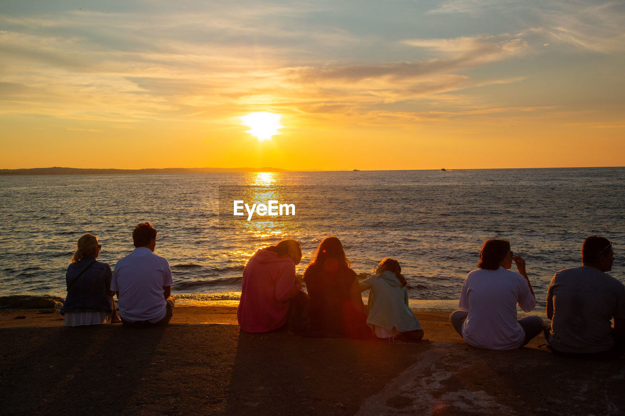 REAR VIEW OF PEOPLE AT SEA DURING SUNSET