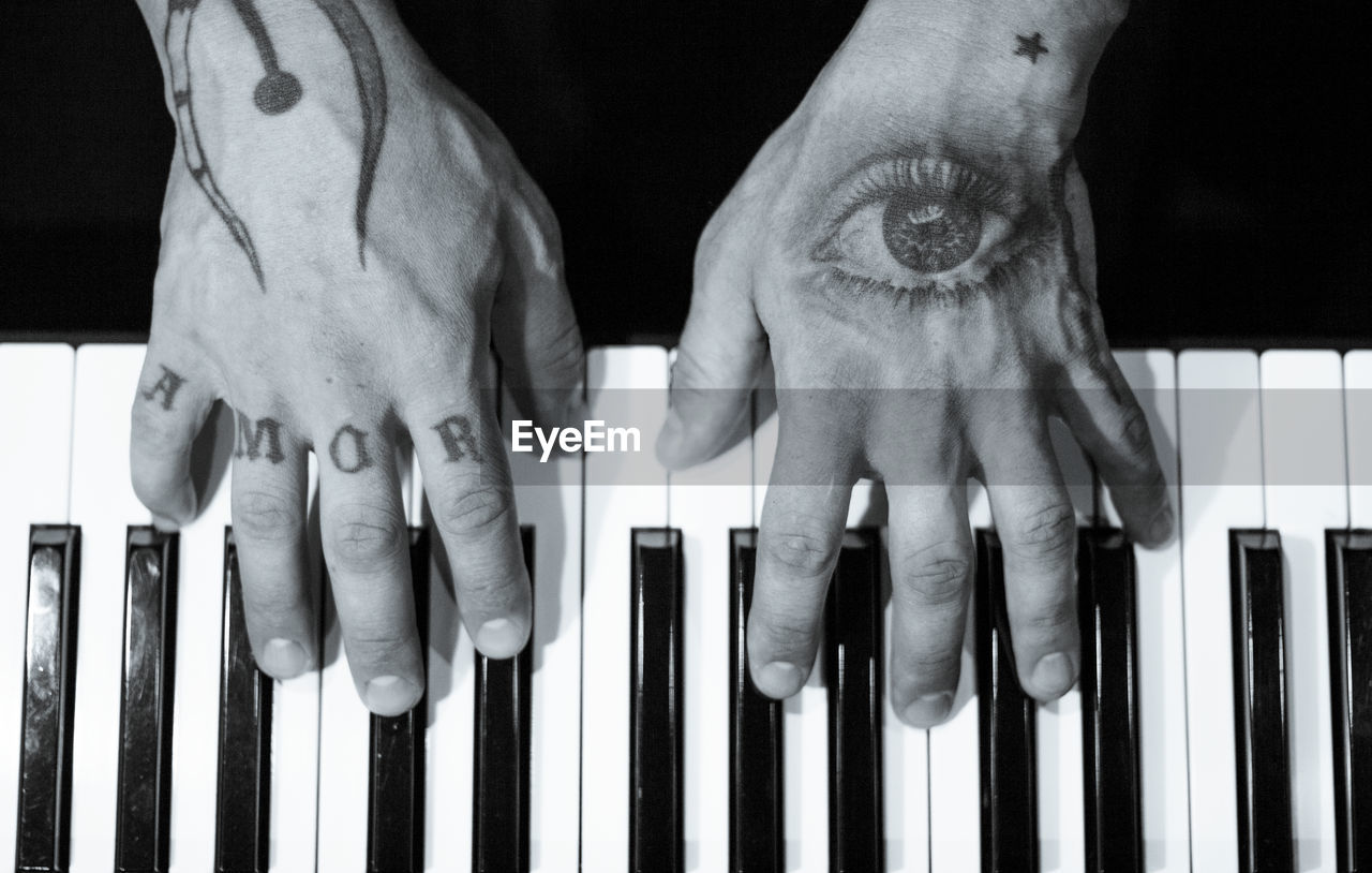 Tattooed mans hands on the keyboard of a piano. dark background