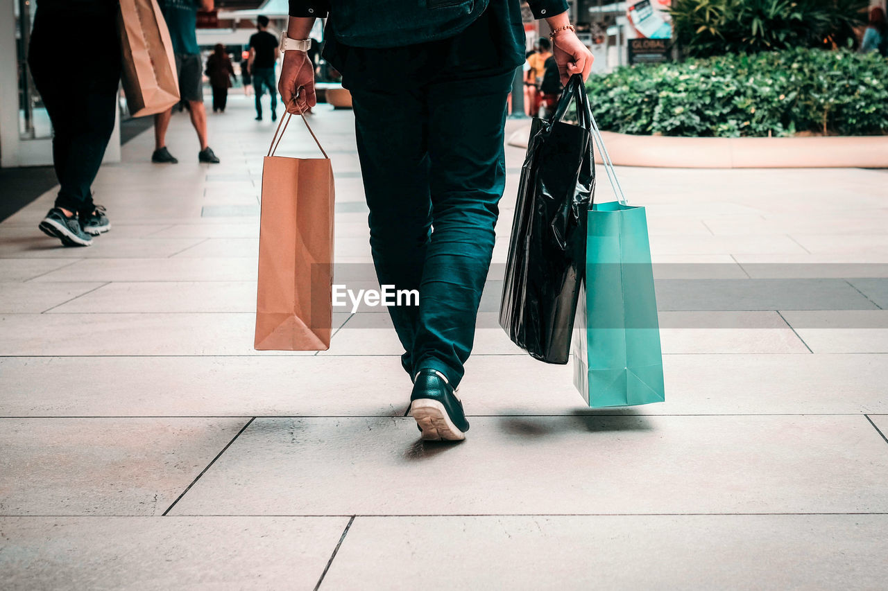 Low section of man with bags walking on sidewalk