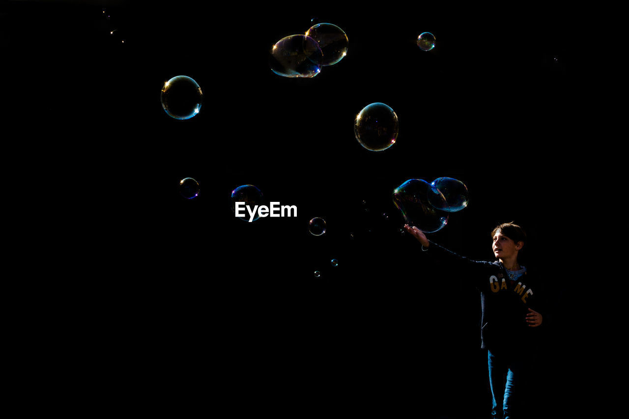 Man touching bubbles while standing against black background