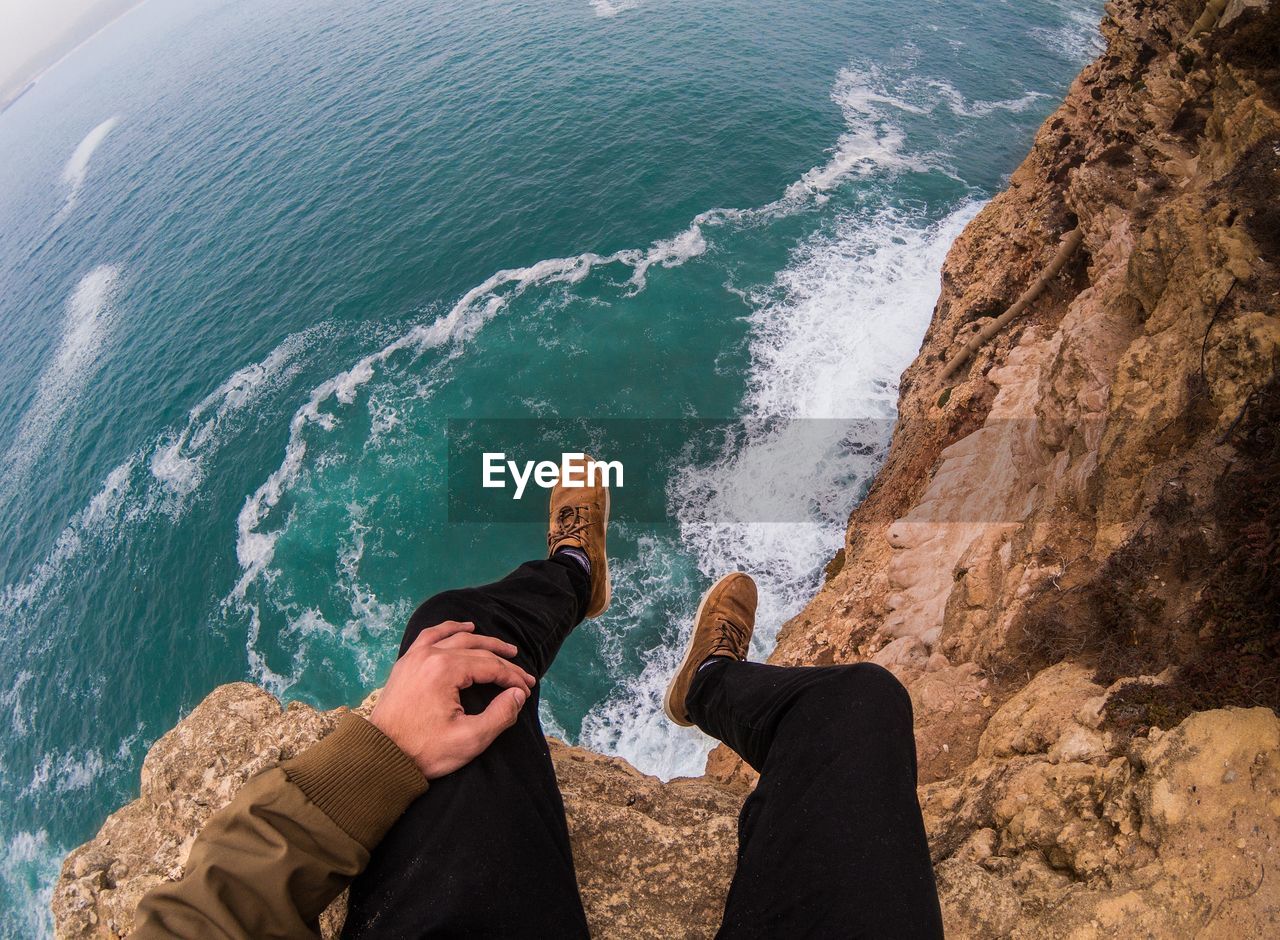 Low section of men sitting on cliff over beach