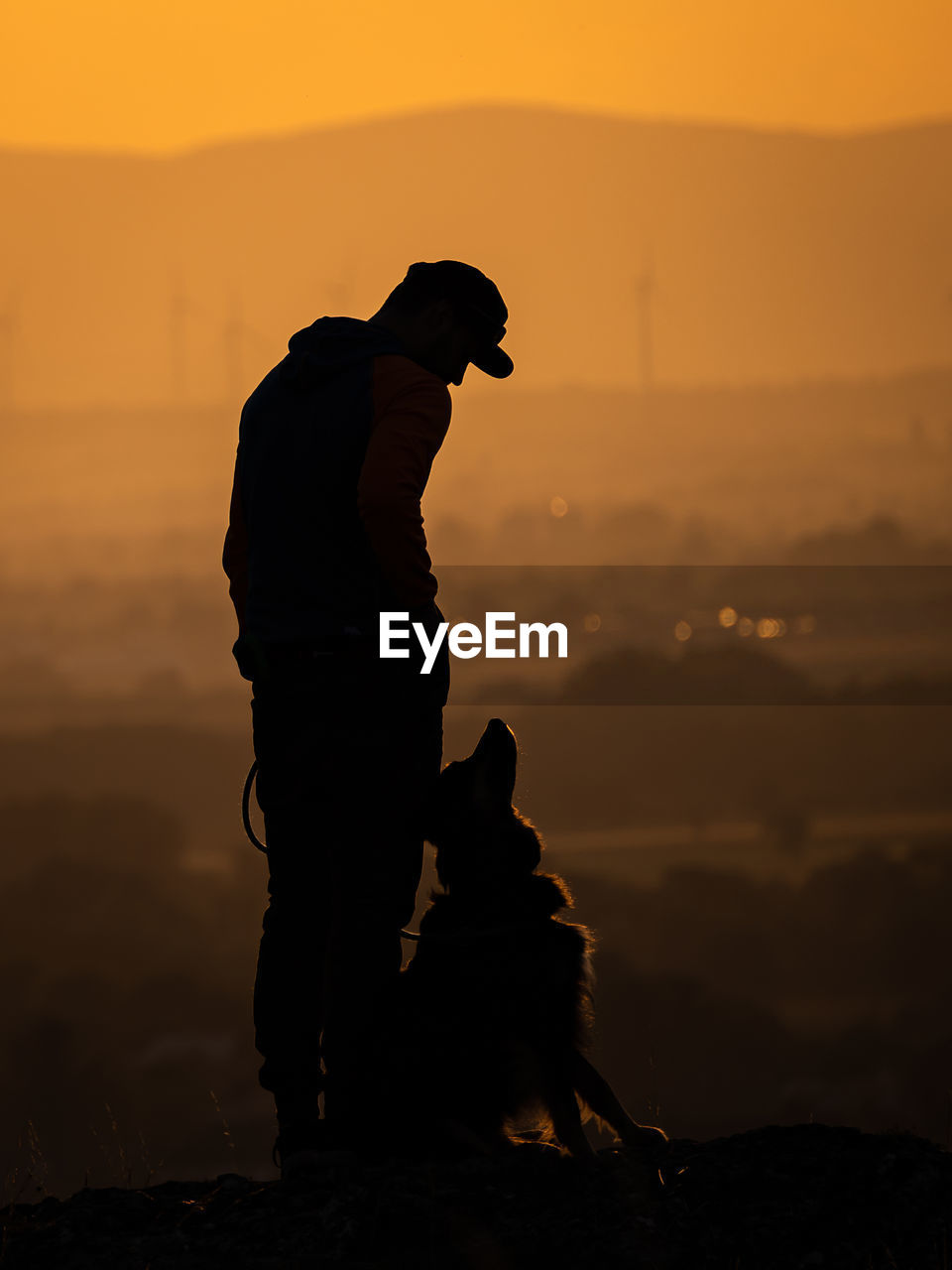 silhouette man with dog on beach against orange sky during sunset