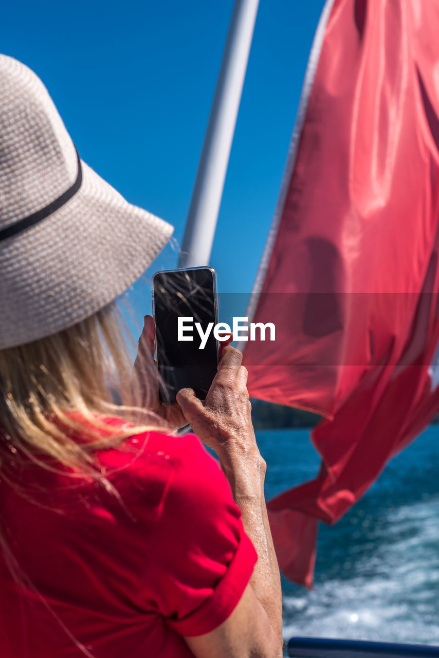 Blonde woman in white cap and red t-shirt taking a photo with the smartphone to the swiss flag.