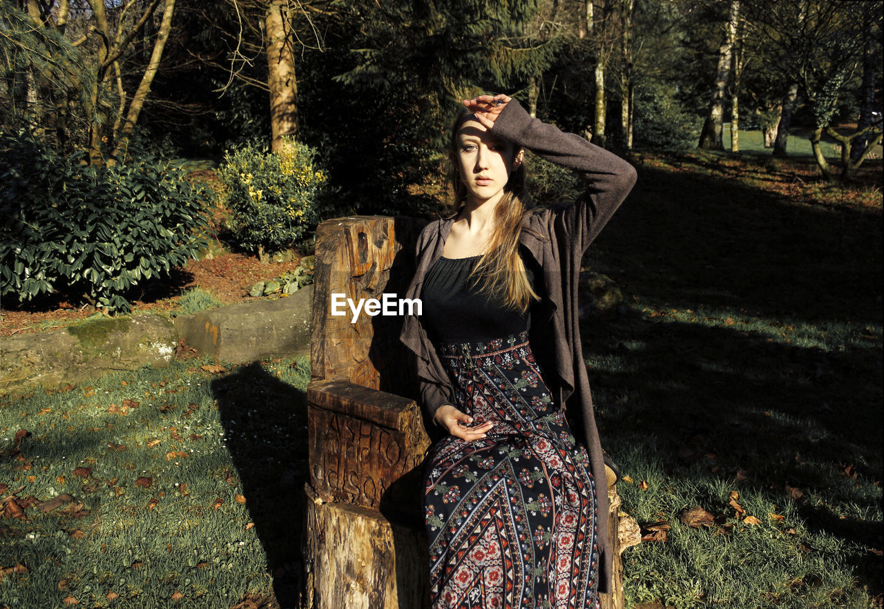 Portrait of young woman sitting on seat in forest