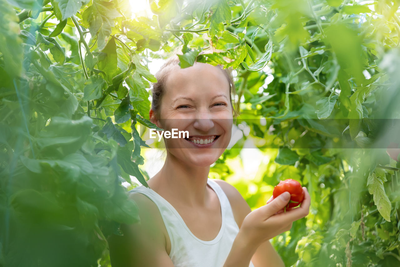 Portrait of young woman holding tomato amidst plant
