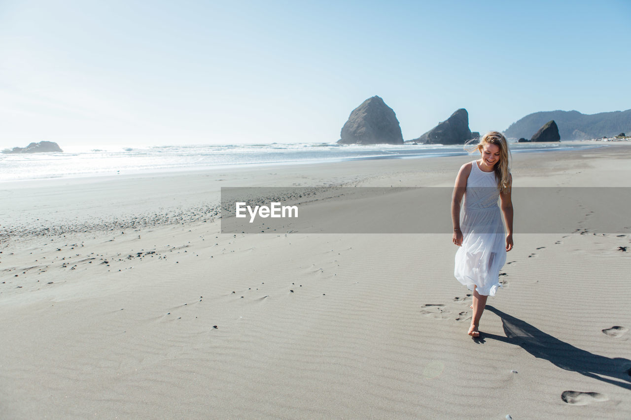 Smiling young woman walking on beach against clear sky