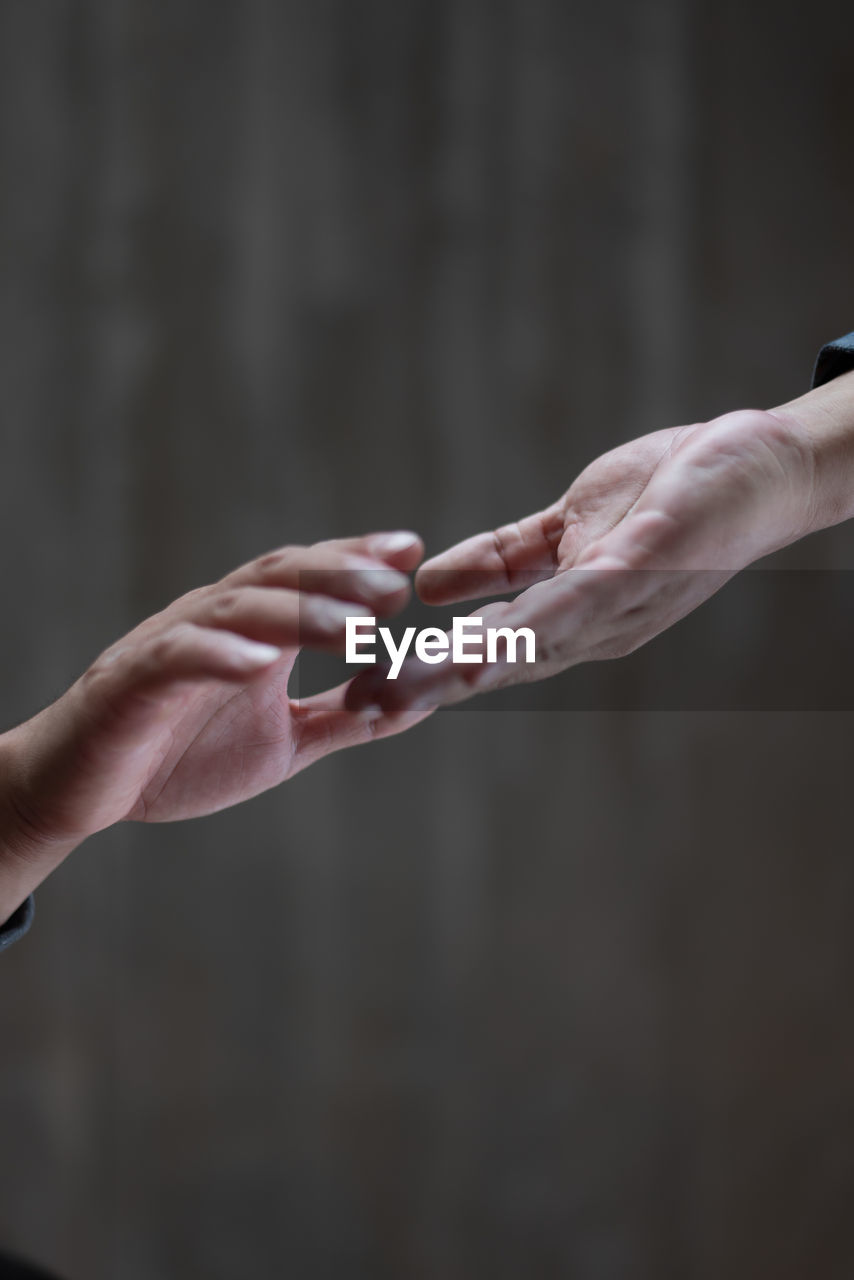 Cropped image of couple holding hands against wall