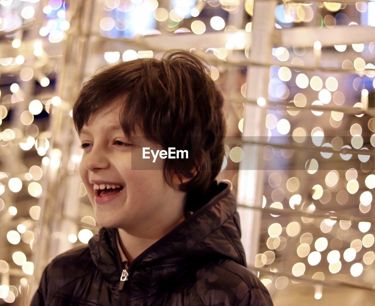 Close-up of cheerful boy looking away against illuminated lights