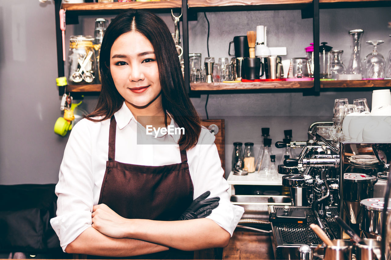 Portrait of female barista with arms crossed standing in kitchen at cafe