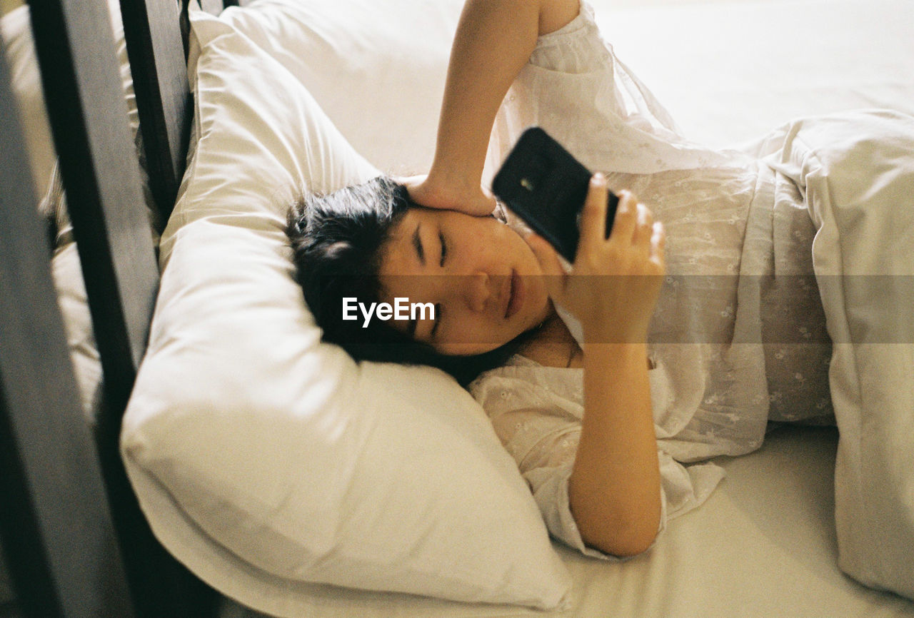 Woman using mobile phone while sleeping on bed at home