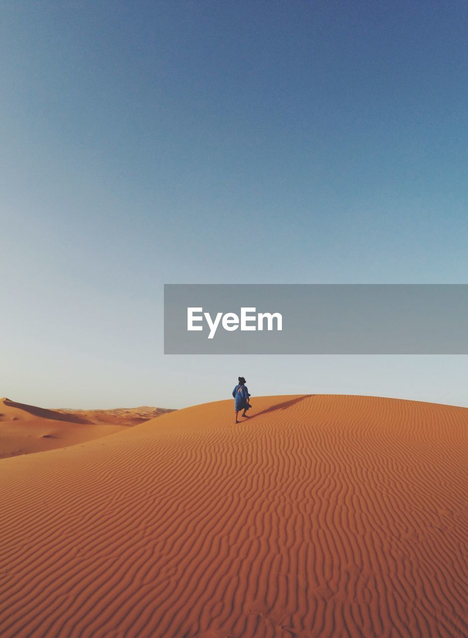 Man walking in desert against clear blue sky