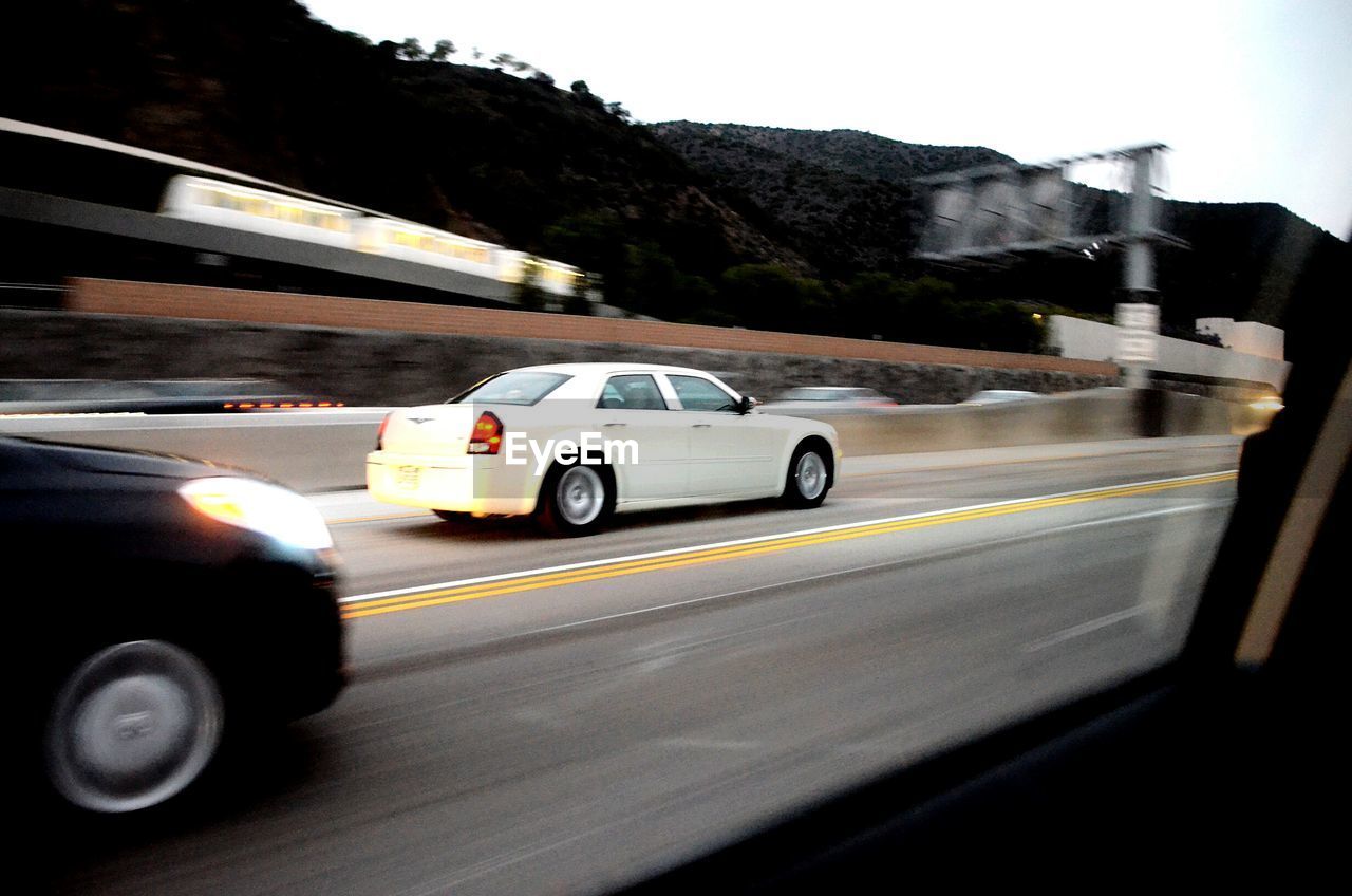 CARS MOVING ON ROAD AGAINST SKY