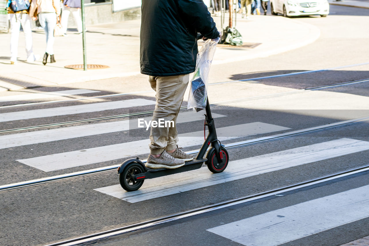 Low section of man riding electric push scooter on city street