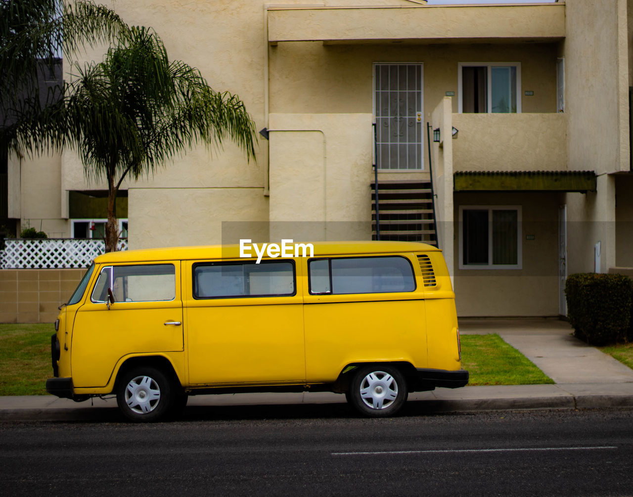 YELLOW CAR PARKED ON STREET AGAINST BUILDINGS