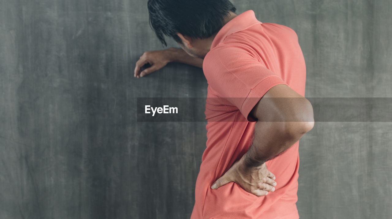 REAR VIEW OF MAN WITH ARMS OUTSTRETCHED STANDING AGAINST WALL