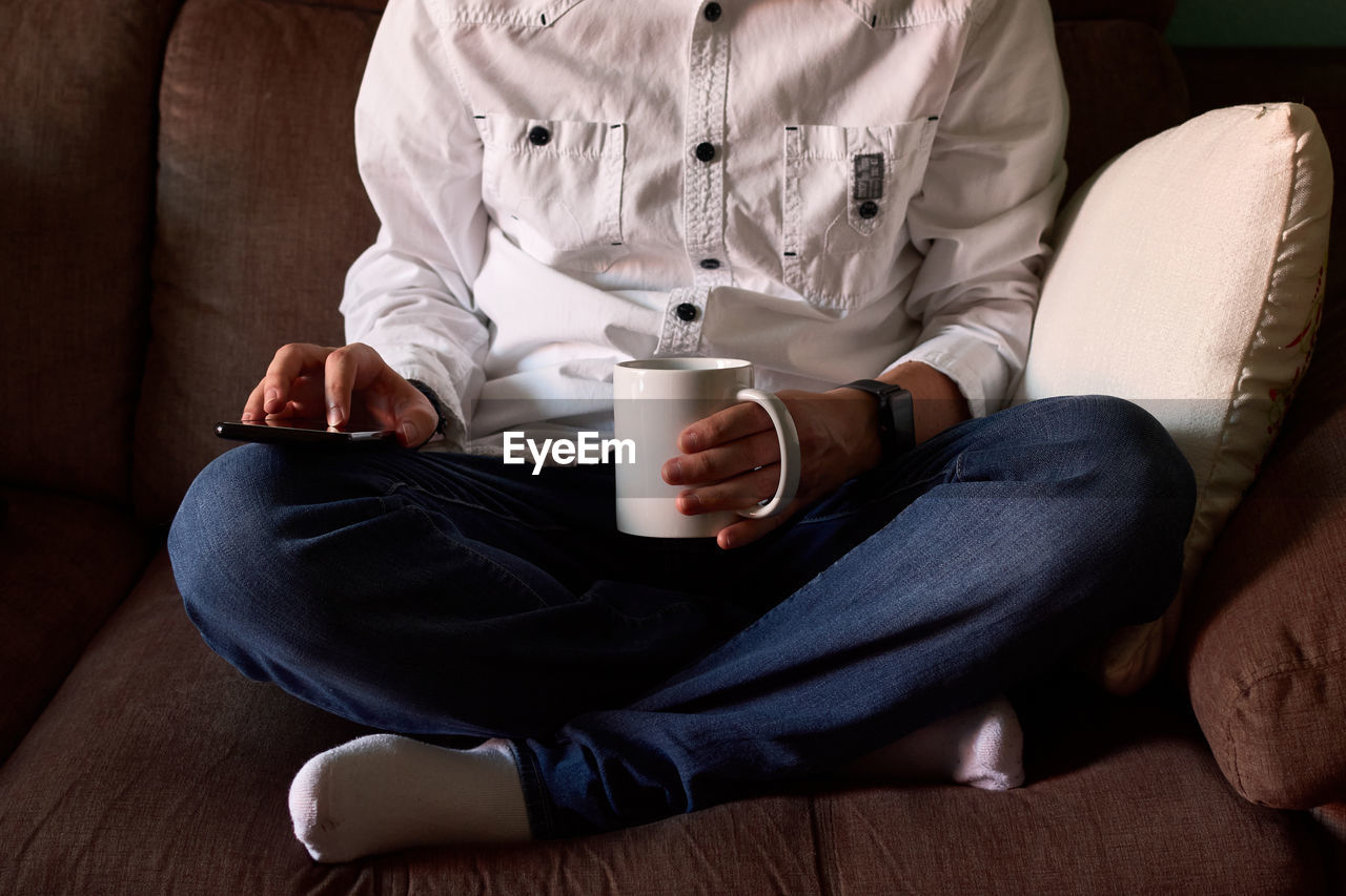 Close-up of a young man looking at his smartphone sitting on a couch