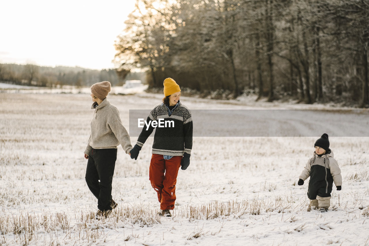 Gay couple holding hands while walking with daughter on snow during winter