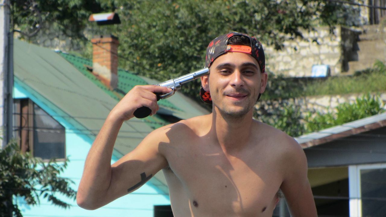 Playful young man pointing gun on his head outside houses